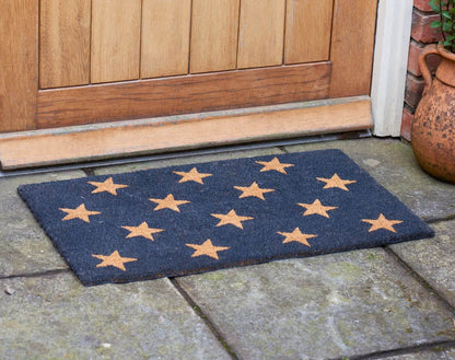 Stars coir doormat with tan star pattern on a stone step by a wooden front door