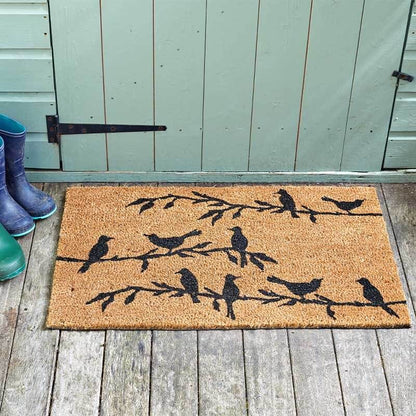 Bird song coir doormat with black bird silhouettes on branches, on a wooden deck by a shed door