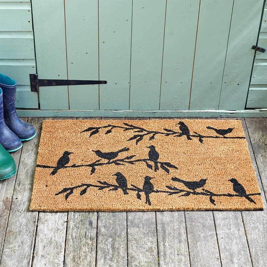 Bird song coir doormat with black bird silhouettes on branches, on a wooden deck by a shed door