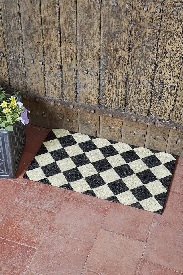 Black and white checkered coir doormat with diamond pattern on a brick step by a wooden door