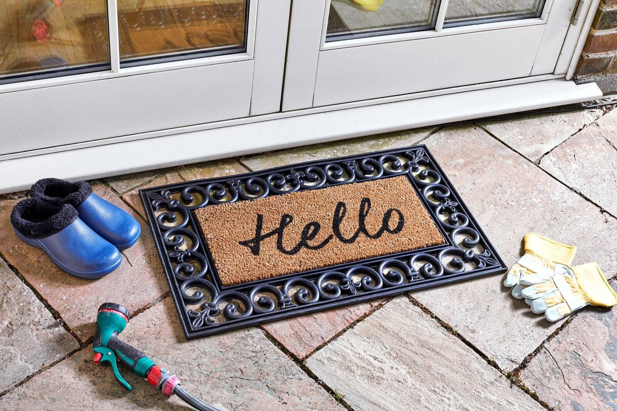 Hello welcome mat coir insert with black script lettering in rubber frame outside a patio door, with wellington boots and gardening gloves
