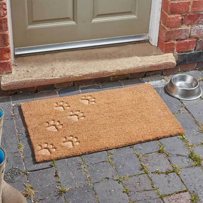 Paw prints embossed coir doormat with tonal paw print design on a brick step by a front door, with a dog bowl