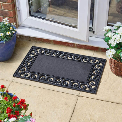 Black rubber doormat frame with scrollwork border outside a patio door, with potted flowers