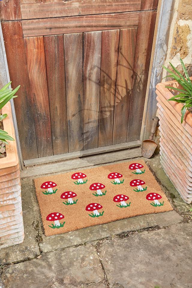Shrooms mushroom coir doormat with red toadstool print on a stone step by a wooden door