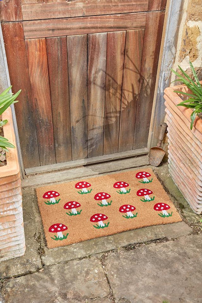 Shrooms mushroom coir doormat with red toadstool print on a stone step by a wooden door