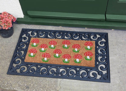 Shrooms coir doormat insert with red toadstool mushroom print in rubber frame outside a front door, with a potted flower