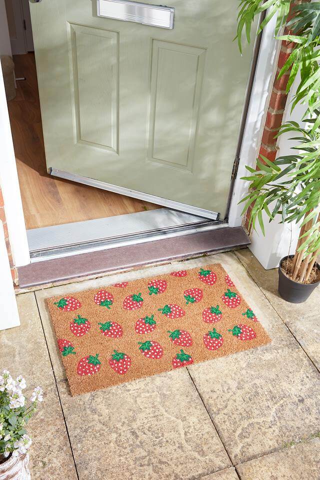 Strawbs coir doormat with strawberry print on a stone step by a front door