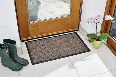 Framed mocha Ulti-Mat washable indoor doormat on a tiled floor by a front door, with wellington boots