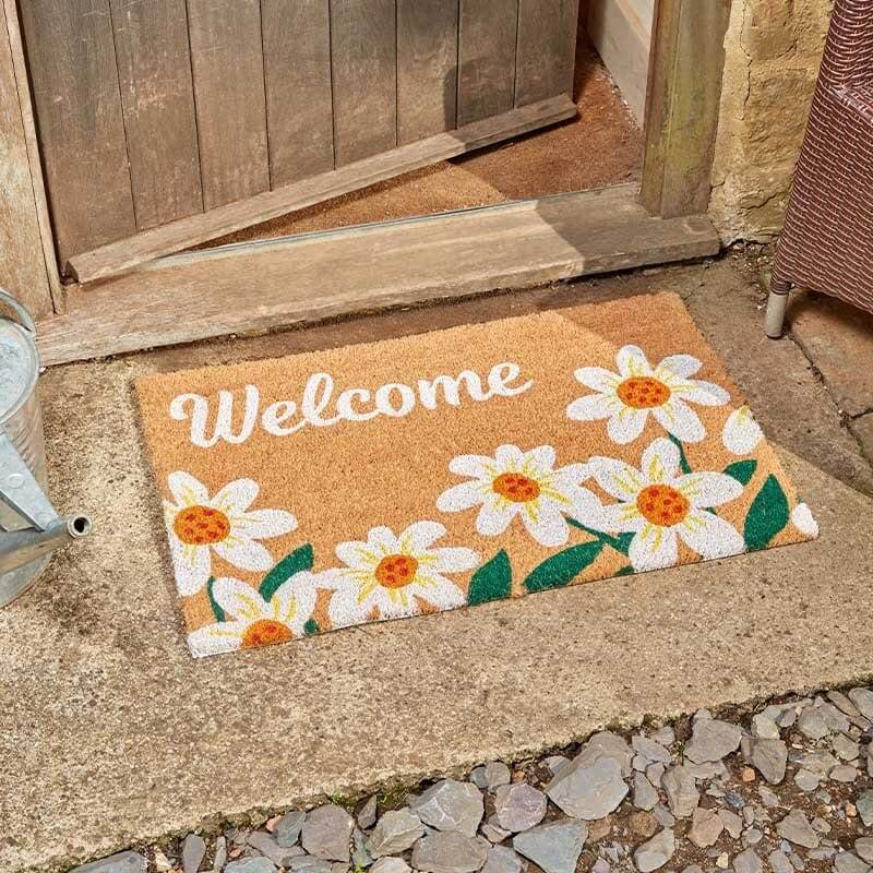 Welcome daisy coir doormat with white daisy flower border on a stone step by a wooden door